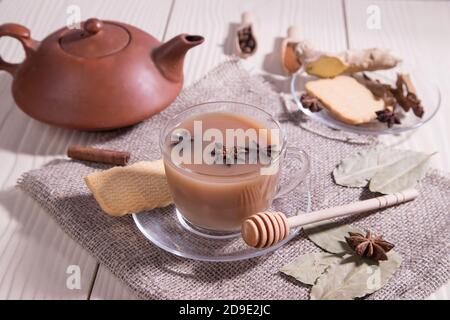 Masala tea-Indian invigorating tea with milk and spices on a white background with a napkin in a glass Cup and a ceramic teapot. Horizontal Stock Photo