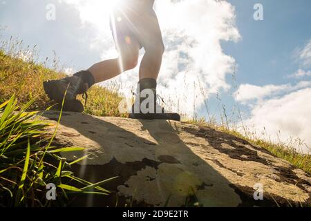 Side portrait woman walking with hiking boots against sunny background Stock Photo