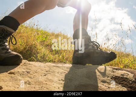 Side portrait woman walking with hiking boots on rock against sunny background Stock Photo