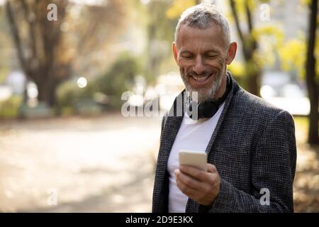 Cheerful handsome man standing outdoors and using smartphone Stock Photo