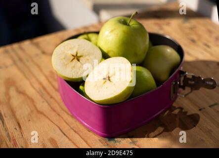 Green apples, whole and halved in a baking dish on a wooden table top. Stock Photo