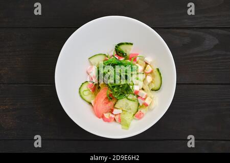 Salad with crab meat, seaweed, tomato, cucumber and sesame on dark wooden table Stock Photo