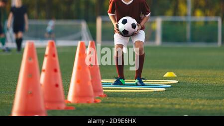 Close up boy running on football training pitch with ball in his hands. Player jumping over obstacles. Football training obstacle course. Children lev Stock Photo