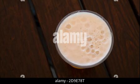 Beer foam in a glass on a wooden table. View from above. Circle made of foam on a dark background. Copy space for text. Stock Photo