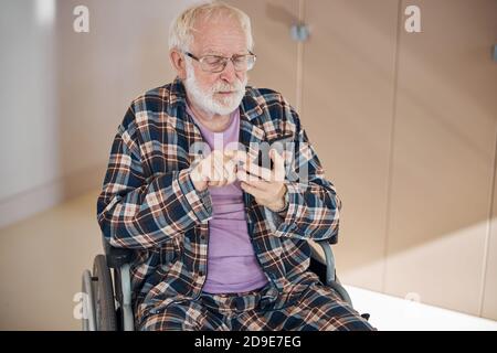 Concentrated gray-headed man texting on his smartphone Stock Photo