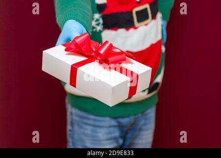 Close up cropped shot of male hands holding white gift box on red studio background.Christmas concept. Stock Photo