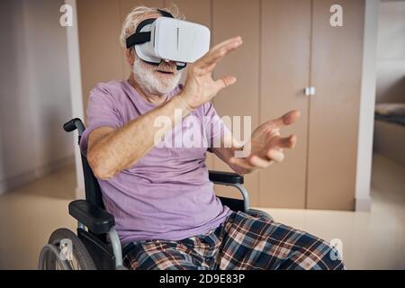 Elderly gamer in VR goggles sitting in the wheelchair Stock Photo