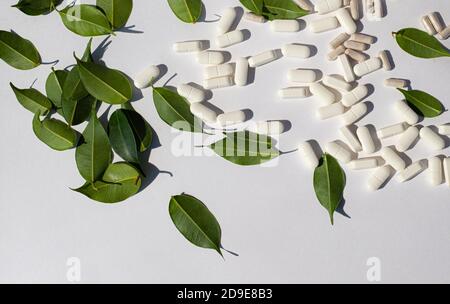 Green leaves and pills are scattered on a light background. Nutritional supplements. Minerals Trace elements in capsules. Stock Photo