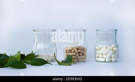 Three glass jars with different capsules. Nearby are green leaves. Copy copy for text. Stock Photo