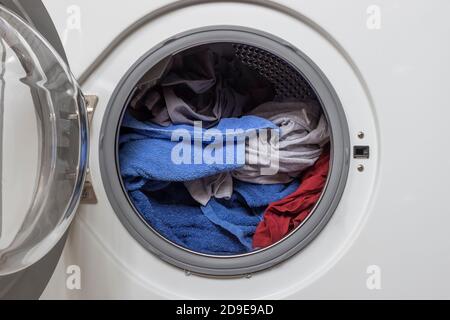 Open door in washing machine with laundry inside. Stock Photo