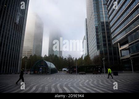 People walk through a nearly deserted Montgomery Square in Canary Wharf, London during foggy conditions at the start of a four week national lockdown for England. Stock Photo