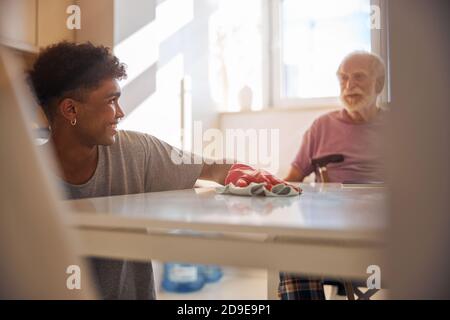 Dark-haired volunteer cleaning the disabled man kitchen Stock Photo