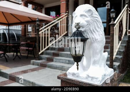 White lion statue holding an old lantern in front of a hotel or restaurant facade. Stairs in the background. Hospitality concept. Sightseeing in east Stock Photo