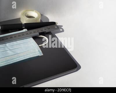 Ballpoint pen ruler sticky tape pencil and medical mask lie on a laptop. Copy space for text. Light background.