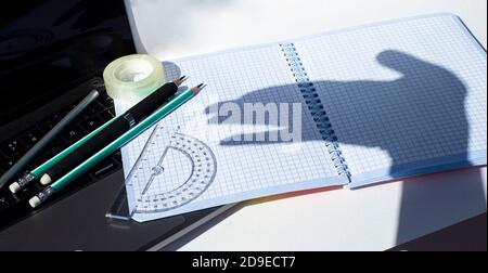 Notebook Stationery and medical masks. On the caged notebook leaves, the shadow from the hands resembles a dog. Difficulties. Rejection. Protest. Stock Photo