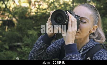 Traveler photographing scenic view in forest. One caucasian woman shooting close up look. Girl take photo video on dslr mirrorless camera. Stock Photo