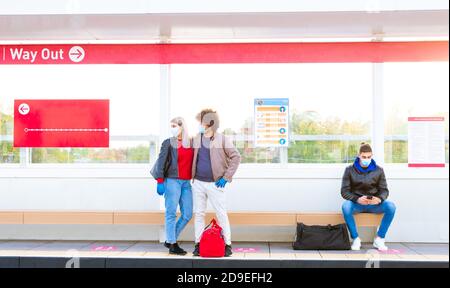 group of a man and a couple wearing protective face mask in a train station waiting for the bus keeping social distances.people standing on a metro Stock Photo