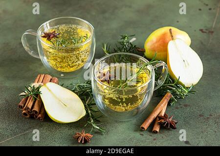 Spicy hot pear or apple cider with cinnamon, anise and rosemary. Traditional autumn or winter drinks. Green concrete background. Stock Photo