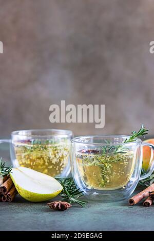 Spicy hot pear or apple cider with cinnamon, anise and rosemary. Traditional autumn or winter drinks. Green concrete background. Stock Photo