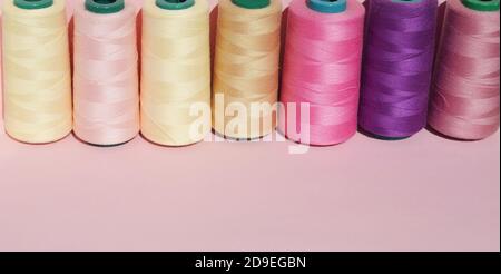 Sewing threads of different colors stand in a row on a pink background. Copy space Banner Stock Photo