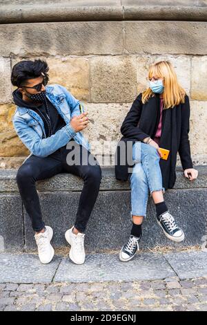 young multi-ethnic couple exchanges information on their mobile phones wearing protective masks during the coronavirus emergency period Stock Photo