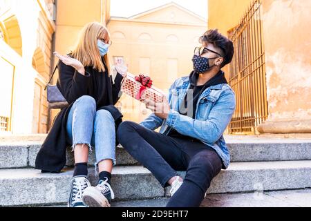 young multiethnic couple exchanges birthday presents wearing protective masks during the coronavirus emergency period Stock Photo
