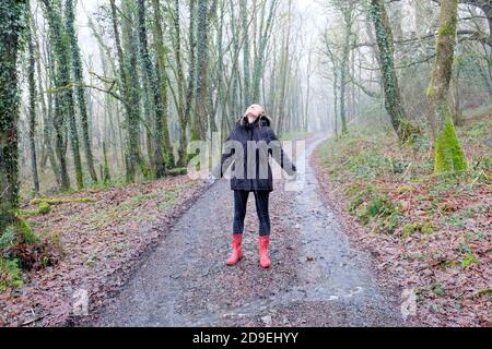 Young happy teen woman wearing winter coat wellies standing in rain day looking up with joy raindrops falling on face in countryside UK  KATHY DEWITT Stock Photo