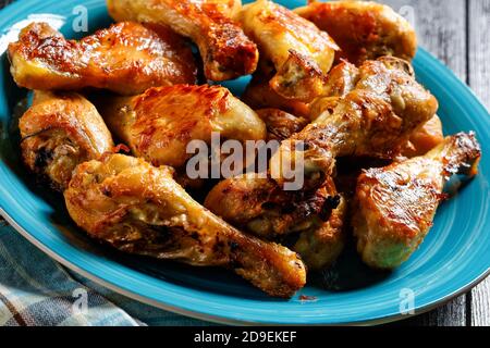 Crispy baked chicken legs drumsticks served on a blue plate on a dark wooden background, top view, close-up Stock Photo