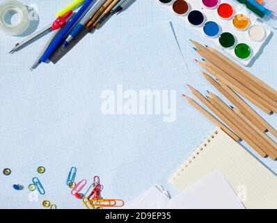 On graph paper, wooden pencils paints paper clips paper paints brushes pens ballpoint tape paper clips and a squared notebook. Copy space for text. Stock Photo