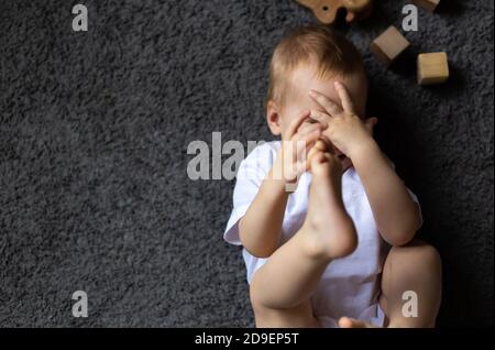 Portrait of baby girl closed his eyes with hands to be invisible or not willing to see, playing fun peek a boo lying on his back on the carpet Stock Photo