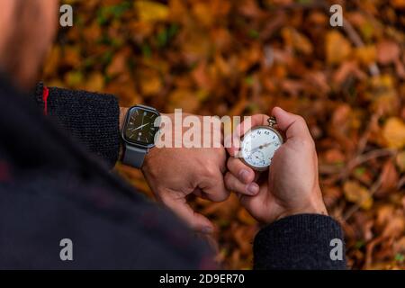 Vintage Pocket watch in man's hand and smart watch on the wrist against the background of autumn dried brown leaves Stock Photo