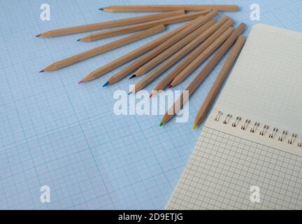 Colored wooden pencils and a notepad in a cage on a blue background. Copy space for text. Stock Photo