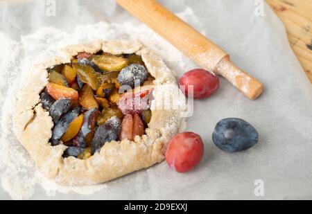 On white baking paper fruit biscuit ripe plums flour and rolling pin. Cooking plum cake. Stock Photo
