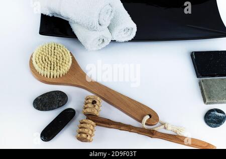 SPA Background with wellness items. Brush for dry body massage. Wooden massager for face and body. Wet white towels on a black ceramic dish.  Stock Photo