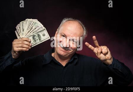 Lucky old man holding with pleasure group of dollar bills Stock Photo