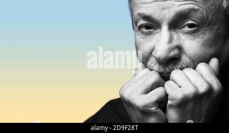 Lifestyle concept.  Old man. Black and white portrait of senior man prop up the head with his fists on yellow blue gradient background with copy-space Stock Photo