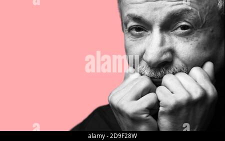 Lifestyle concept.  Old man. Black and white portrait of senior man prop up the head with his fists on coral pink background with copy-space Stock Photo