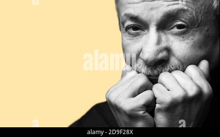 Lifestyle concept.  Old man. Black and white portrait of senior man prop up the head with his fists on yellow background with copy-space Stock Photo