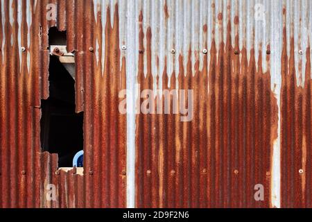 Rusty corrugated metal wall with hole Stock Photo