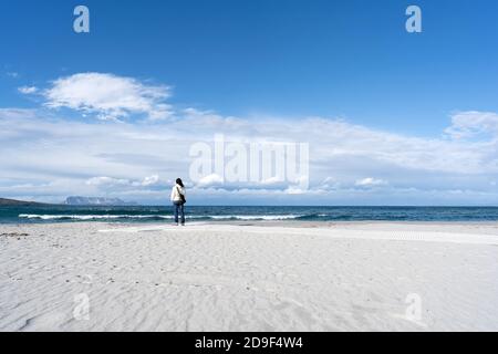 Young unrecognizable woman standing alone by the sea with cloudy sky, looks at the horizon thoughtfully - Pensive single female people in winter on th Stock Photo