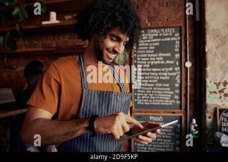 Portrait of confident male barista using digital tablet at counter in cafe