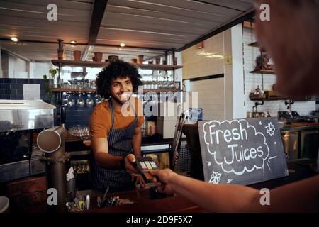 Portrait of smiling waiter holding credit card swipe machine while customer typing code in modern cafe Stock Photo