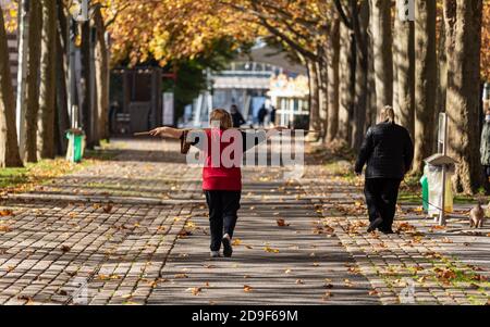 People walking in a parisian park during lockdown in Autumn. A woman is doing stretching exercises with a stick while another is walking her dog. Stock Photo