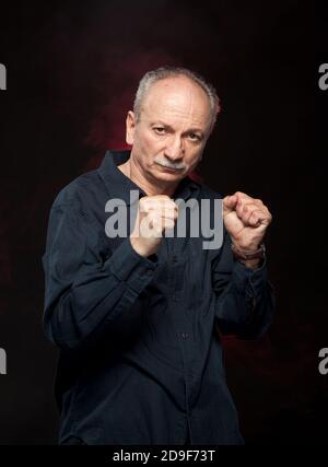 Mature man in boxer pose with raised fists on black background Stock Photo