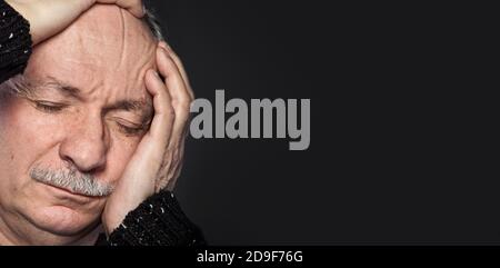 an older man suffering from a headache on dark background Stock Photo