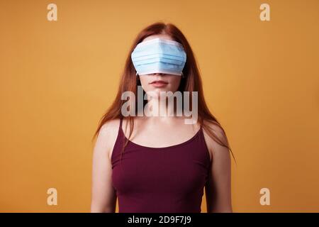 young woman wearing medical face mask over her eyes - funny corona denier concept Stock Photo