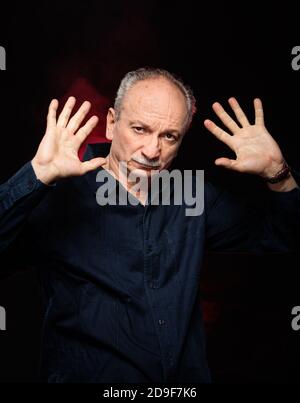 Portrait of elderly man with hands up on a dark background Stock Photo