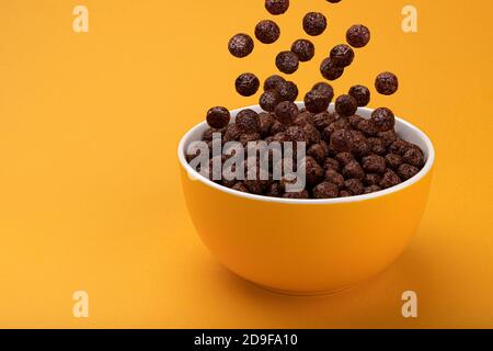 Chocolate Corn balls falling in bowl over yellow background Stock Photo