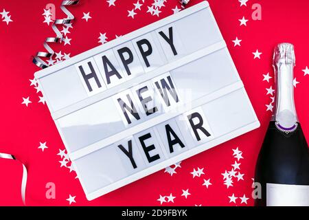 Champagne and lightbox with text Happy New Year on red background Stock Photo