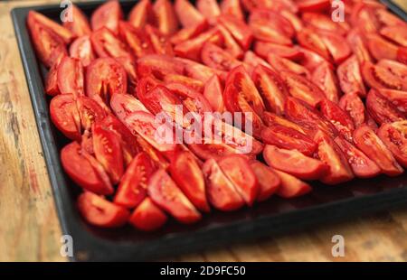 Tomatoes cut into wedges on a black pan. Tomato dishes. Tomato background. Stock Photo